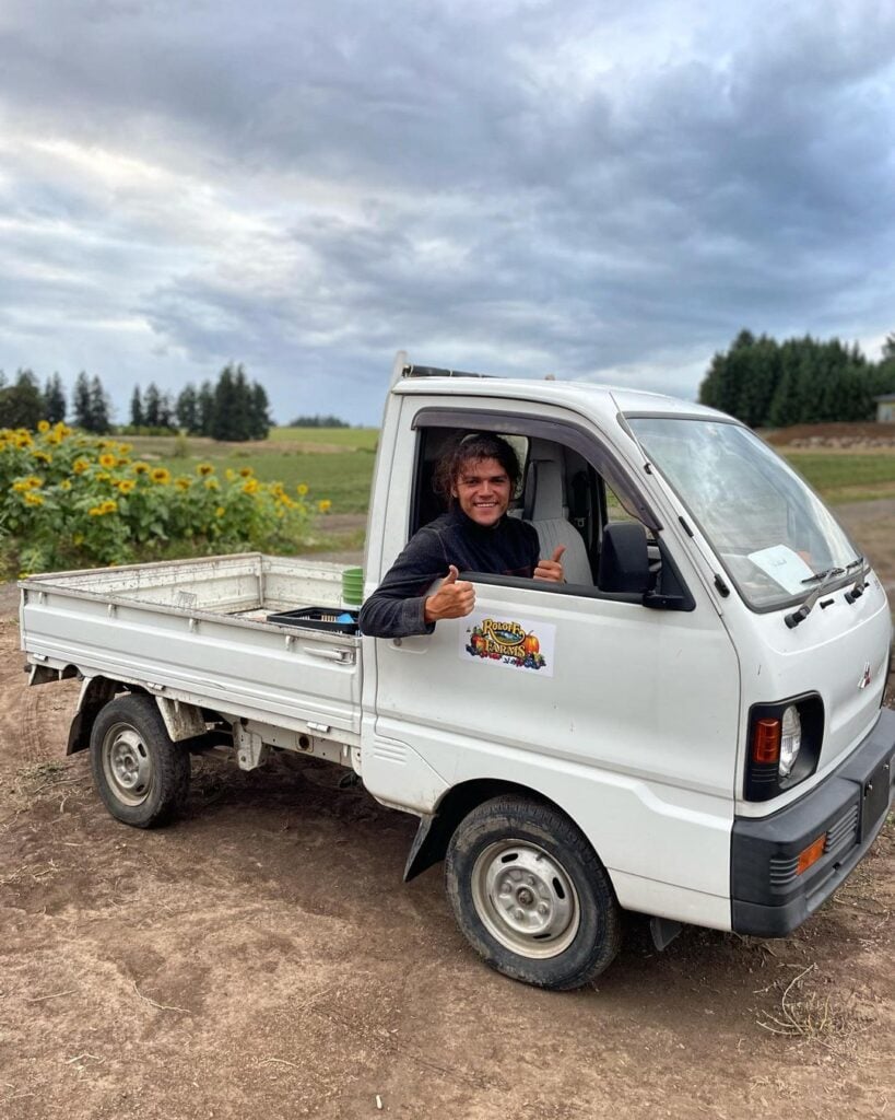 Jocorb Roloff leans out the window of a small, flat-bed farm truck while on Roloff Farms.