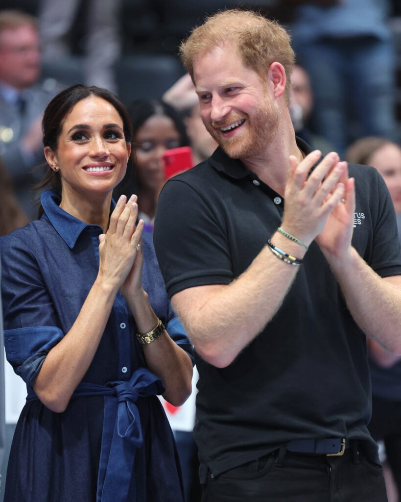 Prince Harry and Meghan Markle clap while standing side by side.