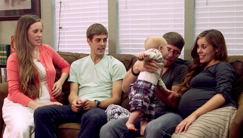 Jill and Jessa Duggar sit on a couch with their husbands between them, one of the men holds a baby