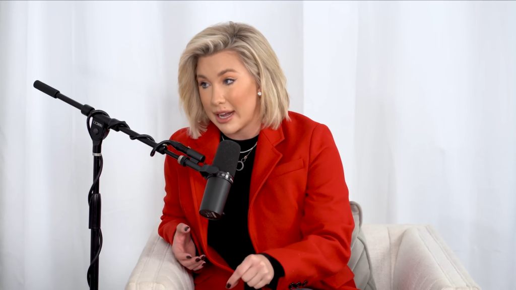 Savannah Chrisley wears a red jacket in a white room. Her hairstyle suggests someone twice her age.